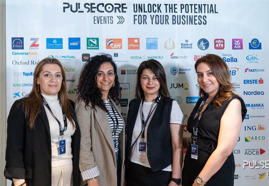 Four delegates standing together in front of the sponsor backdrop at a previous Excellence in Digital Banking summit