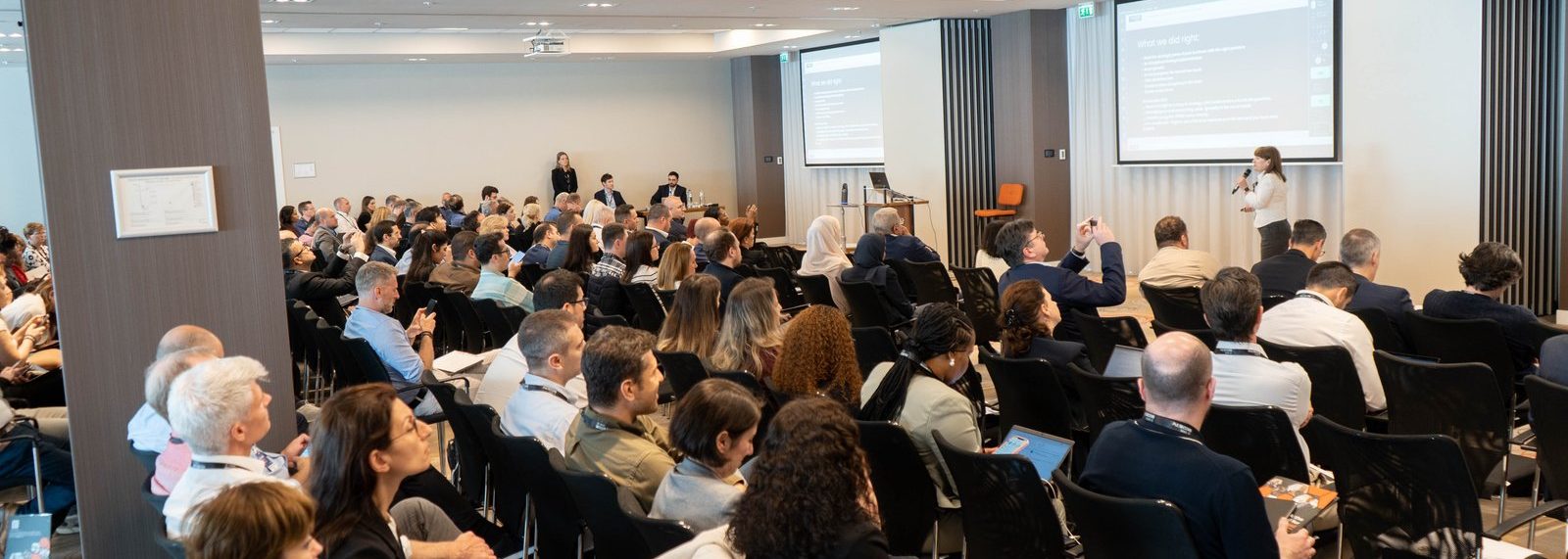 A wide view of the conference room with the audience facing two presentation screens at an Excellence in Digital Banking summit